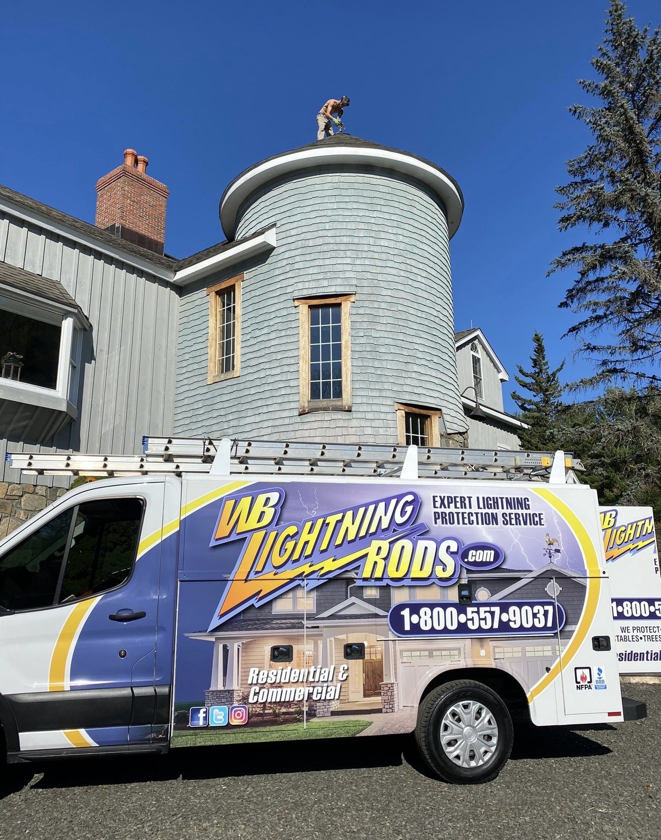 WB Lightning Rods van in front of a shingled estate home with a round turret while a crew member installs a lightning rod on the turret roof